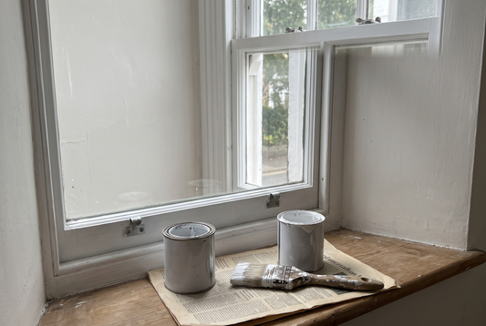 Paint tins and brush on the sill of a freshly painted sash window