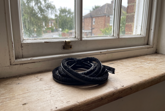 A coil of black brush pile draught seal on a timber windowsill by a double hung sash window