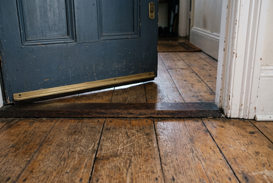 The bottom of a closed timber door meeting a wooden floor, with the gap visible underneath