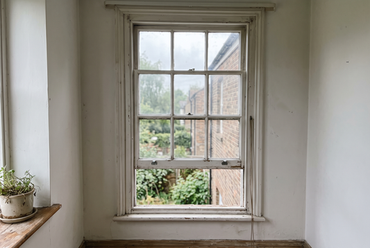 An old white painted timber double hung sash window from inside a room, lower sash raised partway, with a loose sash cord hanging at the side