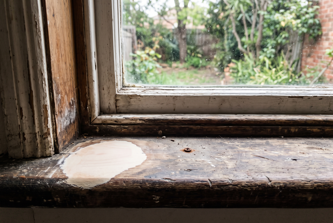 A patch of pale wood repair epoxy sanded smooth into a damaged corner of an old timber window sill.
