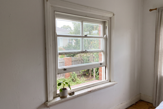 An old white timber double hung sash window in a room looking out to a garden