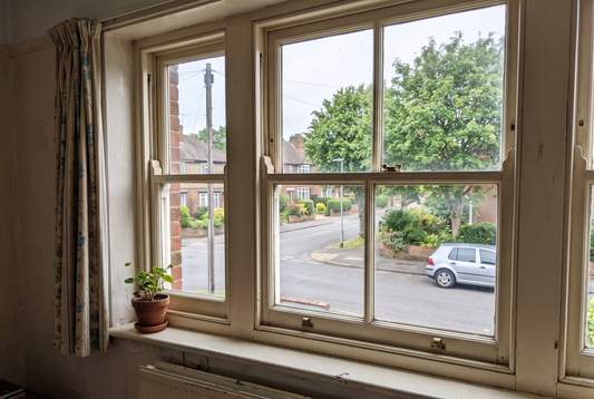Old double hung timber sash window seen from inside a room, looking out onto a quiet street with a parked car