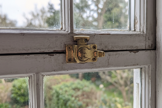 Polished brass sash window lock fitted on the meeting rail of an old white painted timber double hung window