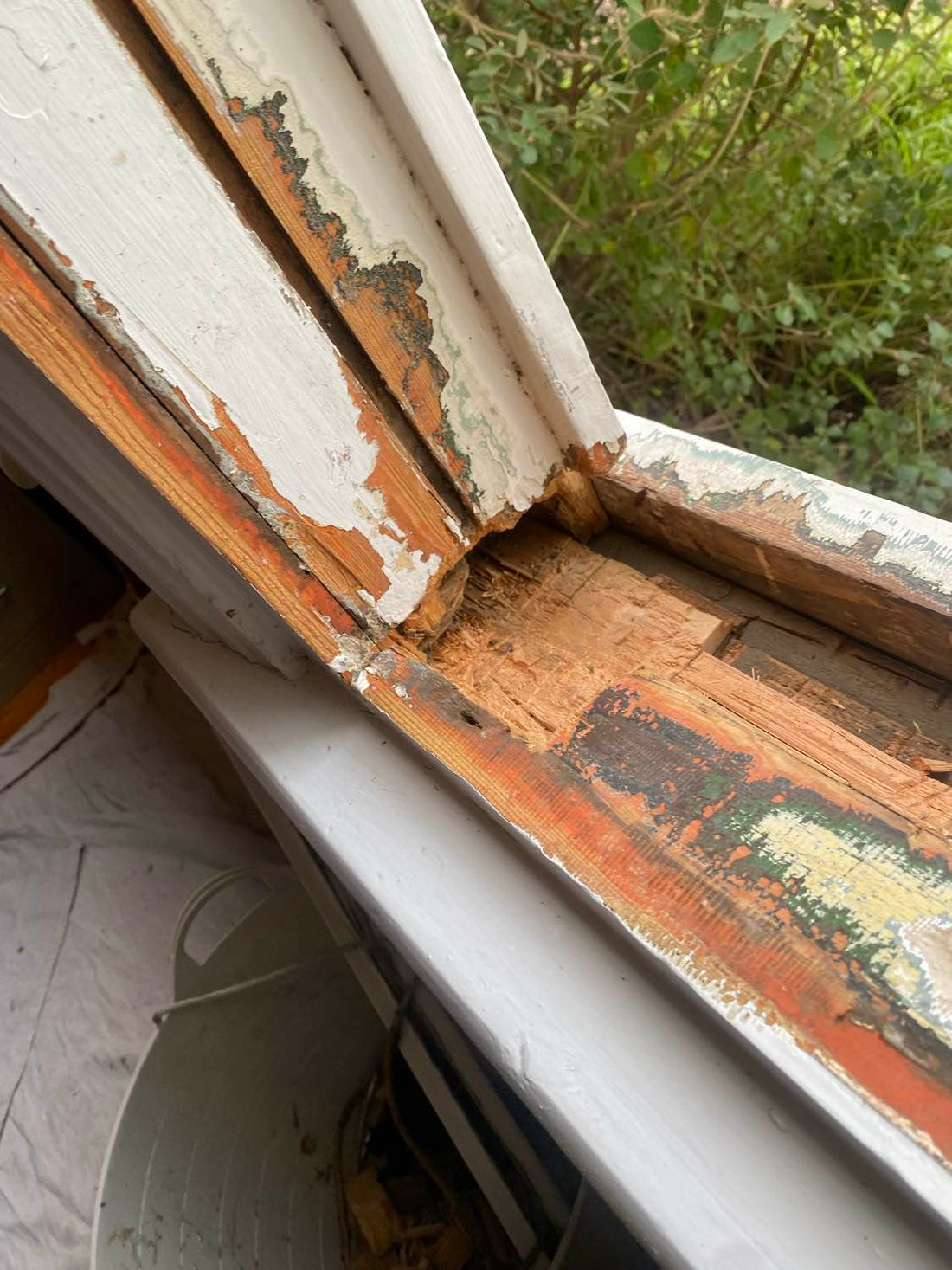 Rotten corner joint on a sash window bottom rail, paint peeling back to expose rotten timber