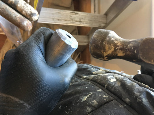 Round extruded lead sash weight held next to an old cast iron sash weight